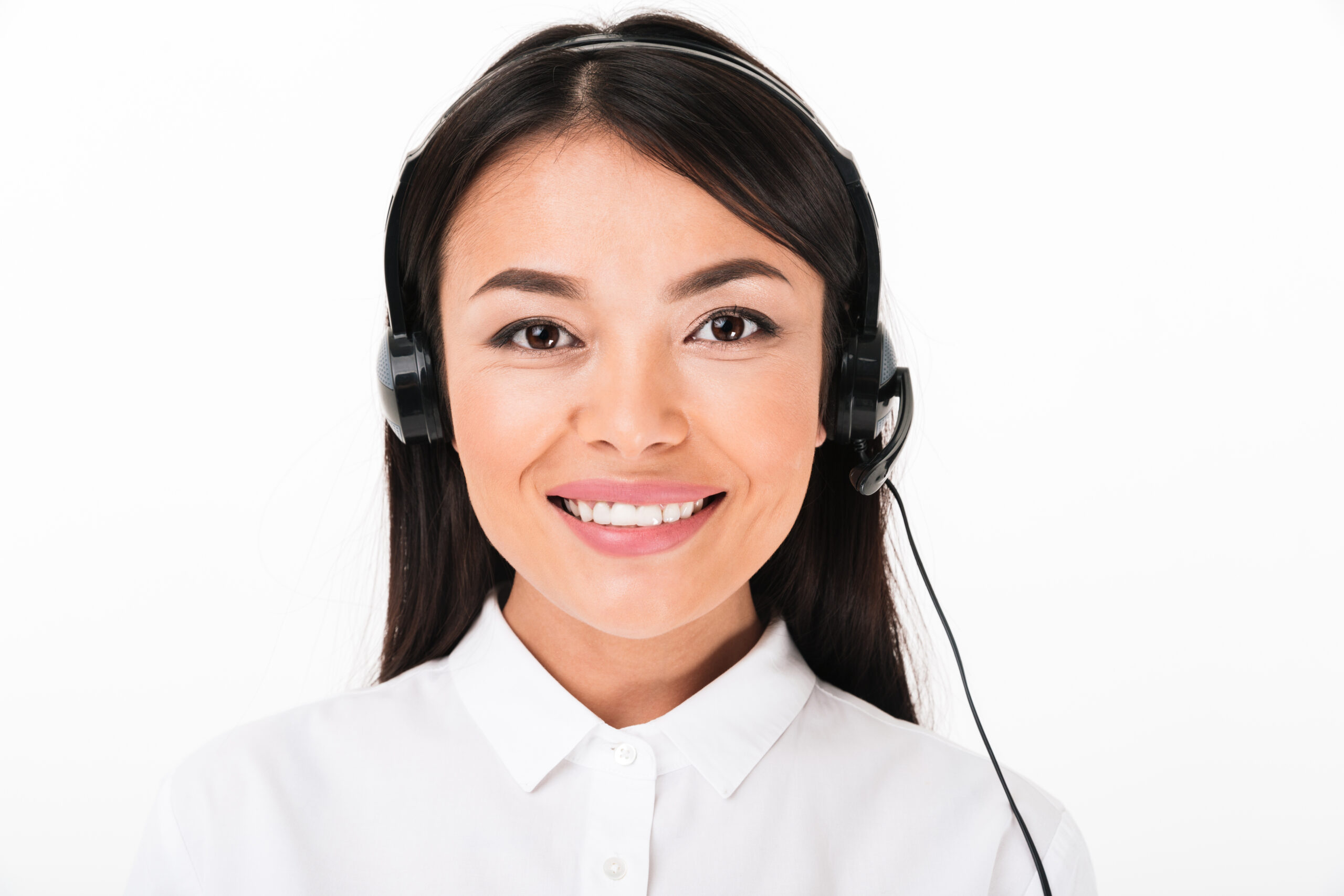 Close up of a friendly asian woman in white shirt wearing headset with microphone isolated over white background
